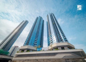 Three glass high rise towers rise into a blue sky with a curved base and palm trees at the entrance am730 logo in the corner