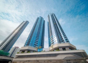 Low angle view of three blue glass skyscrapers rising from a curved multi level podium against a bright sky