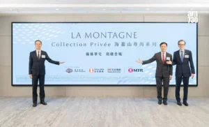 Three men in dark suits pose beside a large light blue banner reading LA MONTAGNE Collection Privée at a corporate event