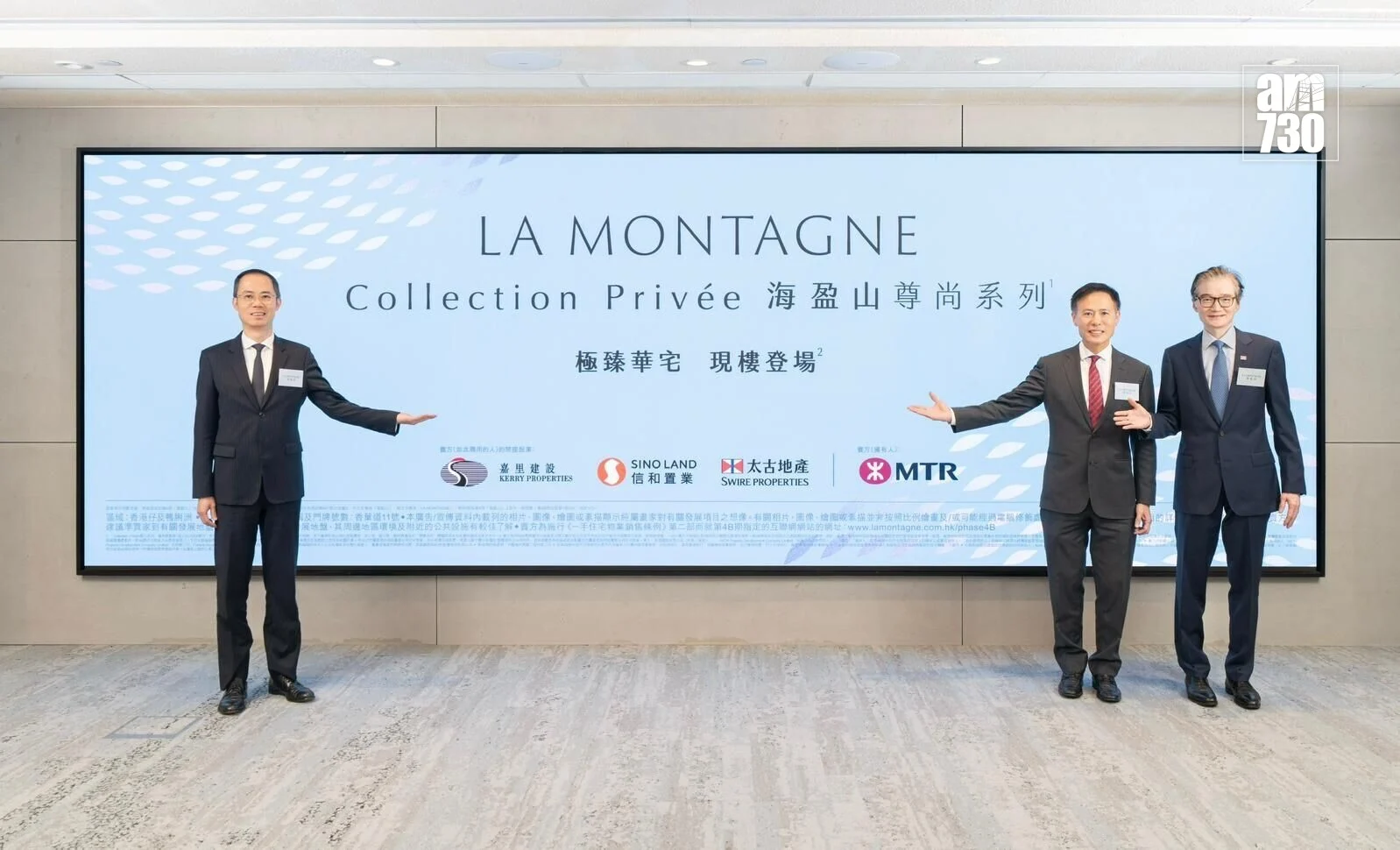 Three men in dark suits pose beside a large light-blue banner reading LA MONTAGNE Collection Privée at a corporate event.