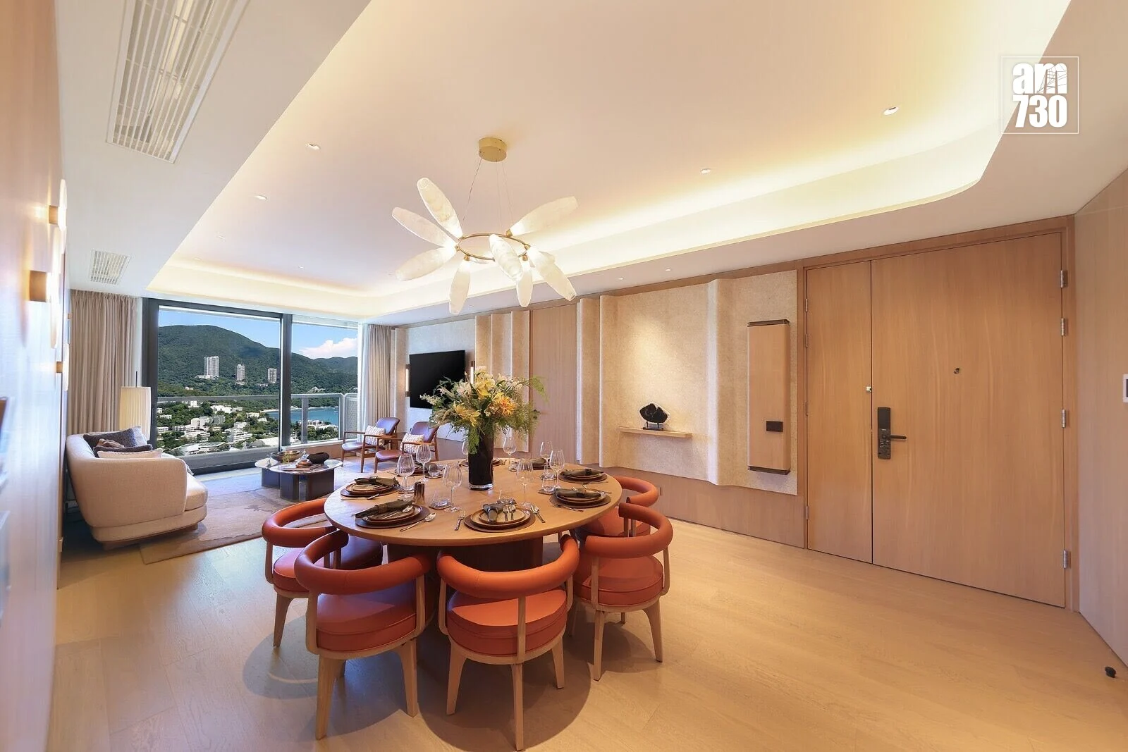 Luxurious dining area with a round table set for eight, peach chairs, and a floral centerpiece, plus a large window showing mountains outside.