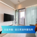 Living room with a wall-mounted TV, balcony door, sheer turquoise curtains, and a gray sofa with an orange pillow.