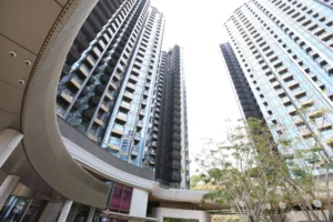 Low angle view of a modern residential complex with tall glass clad towers and a curved ground level arcade Trees appear in the foreground