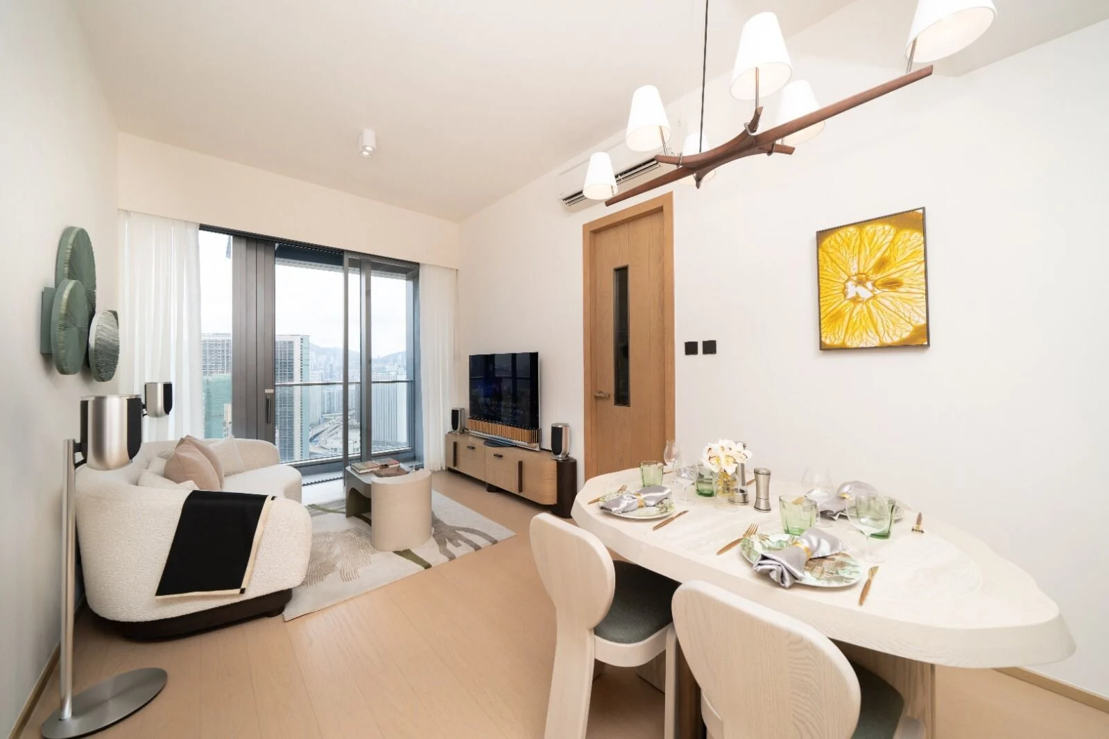 Open-plan living and dining area with a city-view balcony, white furniture, and a yellow flower painting on the wall.