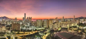 Panoramic city skyline at sunset with an orange to purple sky dense high rise buildings and a foreground sports field