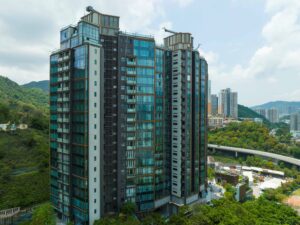 Modern glass clad residential high rise with balconies set against a blue sky and surrounding hills and cityscape