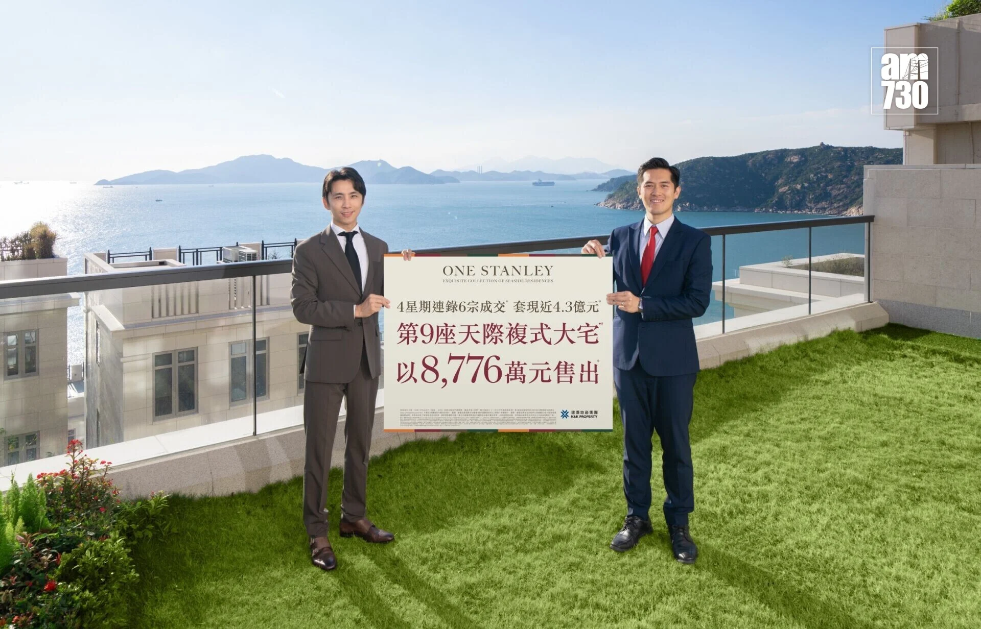 Two professionally dressed men stand on a balcony holding a large real estate poster with Chinese text, overlooking the sea and distant hills, with a logo in the top-right corner.