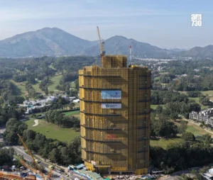 Tall high rise under construction with a crane on top wrapped in yellow safety scaffolding set against green landscape and distant mountains