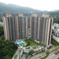Aerial view of a large beige apartment complex with curved towers surrounded by greenery and a swimming pool area at the center mountains in the distance