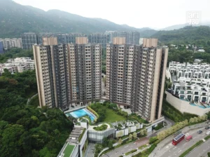 Aerial view of a large beige apartment complex with curved towers surrounded by greenery and a swimming pool area at the center mountains in the distance