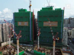 Two under construction high rise buildings covered in green netting with cranes nearby sign reads One Victoria Cove on the right tower