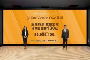 Two professionally dressed individuals stand beside an orange promotional backdrop for One Victoria Cove featuring Chinese text and pricing details