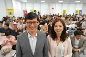Smiling man in a gray suit and a woman in a light blouse pose at the front of a crowded conference room