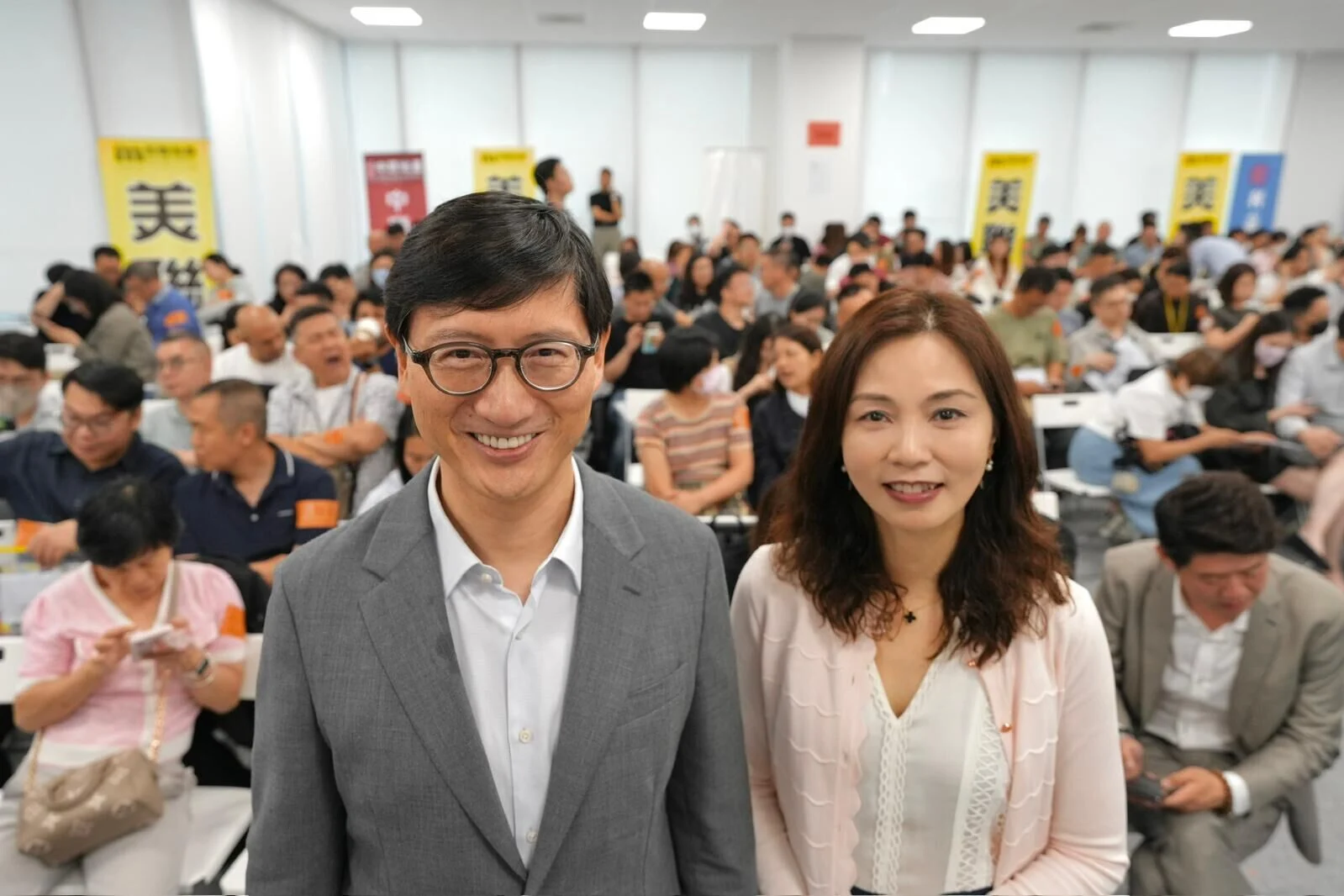 Smiling man in a gray suit and a woman in a light blouse pose at the front of a crowded conference room.
